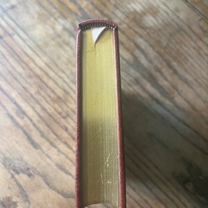 May include: The spine of a hardback book with a brown leather cover and gold-gilded edges.