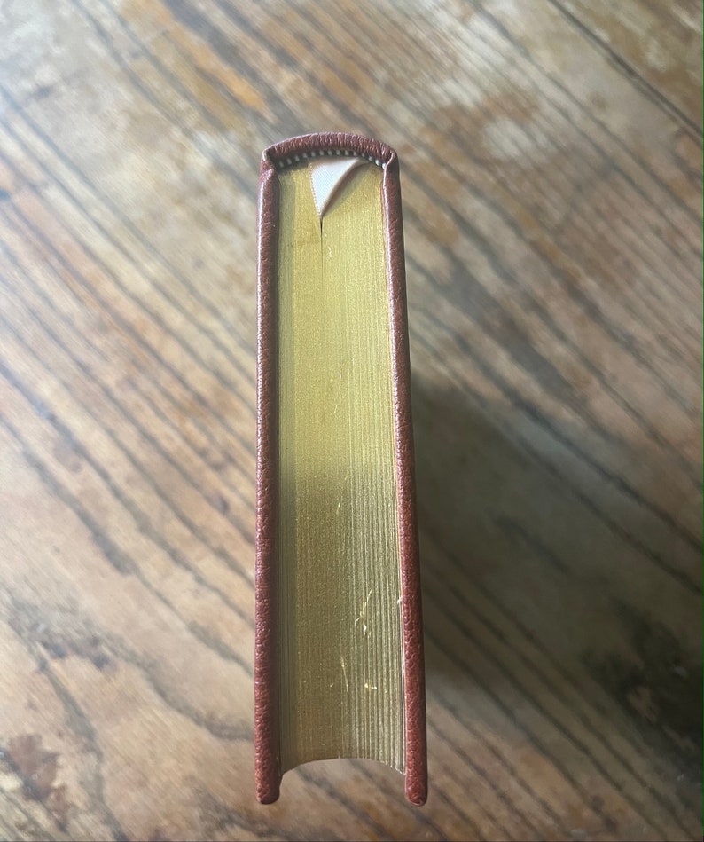 May include: The spine of a hardback book with a brown leather cover and gold-gilded edges.