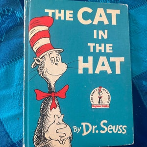 May include: A blue book with the title "The Cat in the Hat" by Dr. Seuss. The cover features a cartoon cat wearing a red and white striped hat and a red bow tie.