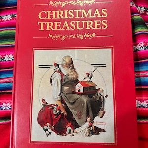 May include: A red hardcover book titled "CHRISTMAS TREASURES" in gold lettering. The cover features a color illustration of Santa Claus surrounded by elves and a doll. The book is on a colorful patterned fabric.