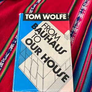 May include: A blue and pink paperback book titled "From Bauhaus to Our House" by Tom Wolfe. The cover features a black and white illustration of a modern house.