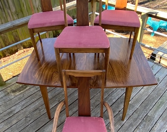 May include: Four wooden dining chairs with pink fabric seats and a matching wooden table. The chairs have a tall, narrow back with a vertical slat design.