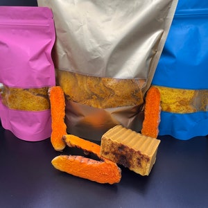 Könnte beinhalten: Drei wiederverschließbare Beutel gefüllt mit Kurkumawurzel, einer rosa, einer goldfarben und einer blauen. In der Mitte des Bildes befindet sich eine Stange Kurkuma-Seife.