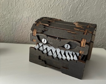 May include: A wooden treasure chest with a menacing face carved into the front. The chest is painted black with white teeth and eyes.
