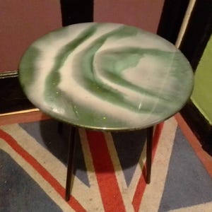May include: A round side table with a green and white epoxy resin top and black metal legs.