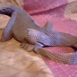 May include: A gray, wooden sculpture of a lizard with a textured, scaly surface.