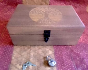 May include: A wooden box with a tree of life design on the lid. The box has a black clasp and a small padlock with a key. The box is rectangular and made of light-colored wood.