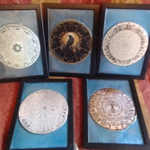 May include: Five framed circular artworks with detailed designs. Each piece has a central motif and surrounding text. The frames are black, and the artwork is set against a light blue background. The artworks appear to be decorative.