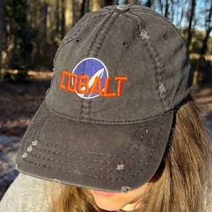 May include: A black distressed baseball cap with a blue and white logo and the word "COBALT" embroidered in orange.