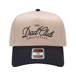 May include: A beige and black baseball cap with the text "The Dad Club Collective" in black script. The cap has a curved brim and a button on top. The label reads "OTTO Classic Fit OSFM Mid Profile".