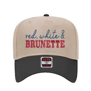 Könnte beinhalten: Beige und schwarze Baseballkappe mit dem gestickten Text "red, white & BRUNETTE" in roter und blauer Schrift. Die Kappe hat einen gebogenen Schirm und einen kleinen schwarzen Knopf oben. Ein kleines Etikett ist sichtbar.