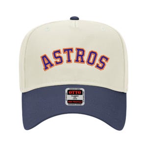 May include: A baseball cap with a cream-colored crown and a navy blue brim. The word "ASTROS" is embroidered in orange and blue arched across the front. The cap has a curved brim and a small tag on the side.