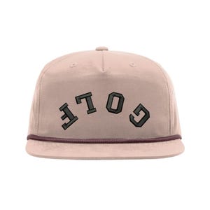 Könnte beinhalten: Hellrosa Cap mit flachem Schirm und dem Wort "GOLF" in dunkelgrauen Blockbuchstaben gestickt. Die Kappe hat eine braune Kordel entlang des Rands.