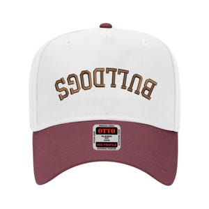 May include: A white baseball cap with a maroon bill and a maroon button on top. The word "BULLDOGS" is embroidered in brown across the front. The cap has a mid-profile fit and is made of premium fabric.
