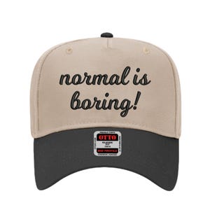 May include: A beige and black baseball cap with the phrase "normal is boring!" embroidered in black script across the front. The cap has a curved brim and a small tag on the side.