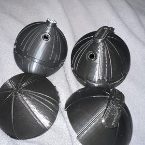 May include: Four black 3D printed sphere halves. Two halves are assembled into spheres with a small hole in the top. The other two halves are separate.