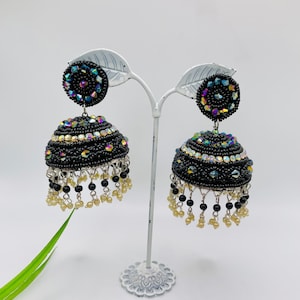 K&ouml;nnte beinhalten: Ein Paar schwarze Jhumka-Ohrringe mit schillernden Steinen und schwarzen Perlen, die unten h&auml;ngen.