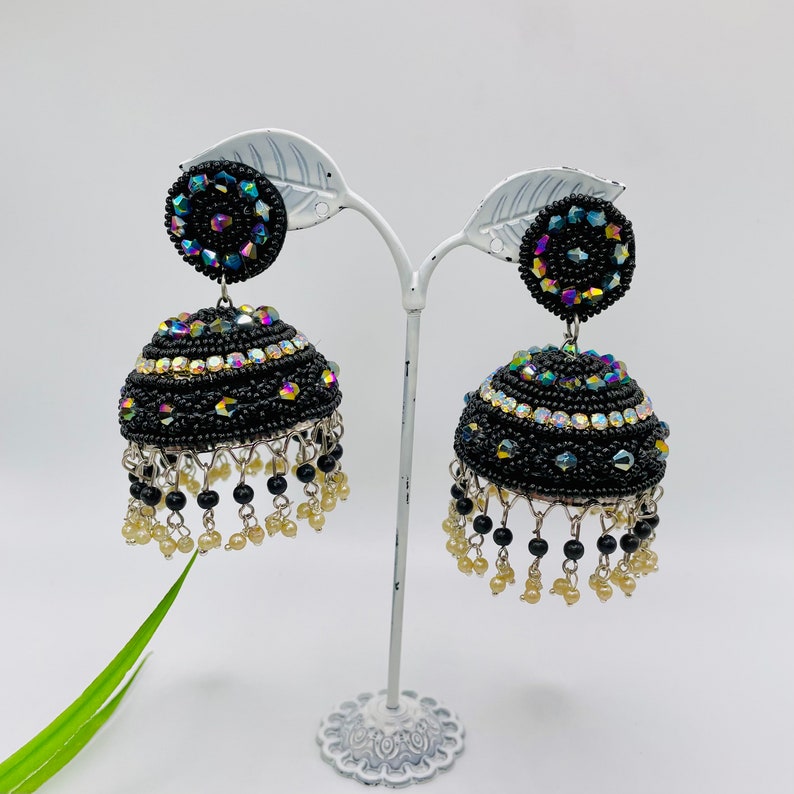 K&ouml;nnte beinhalten: Ein Paar schwarze Jhumka-Ohrringe mit schillernden Steinen und schwarzen Perlen, die unten h&auml;ngen.