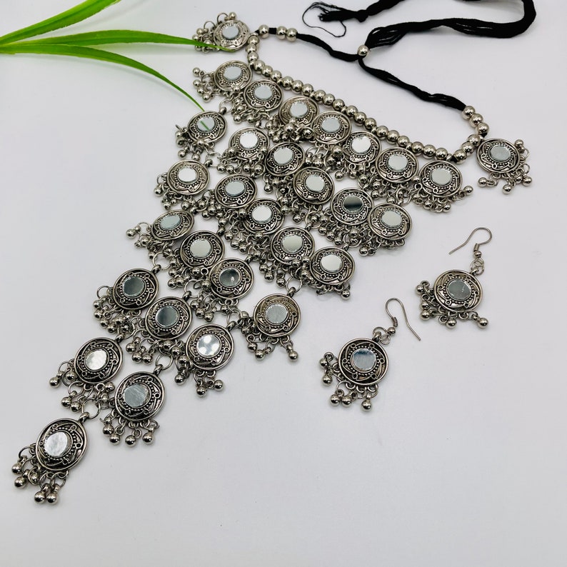 May include: A silver-toned necklace and earring set. The necklace features multiple circular mirrored pendants with dangling accents. The earrings mirror the design. The jewelry is displayed on a white surface.