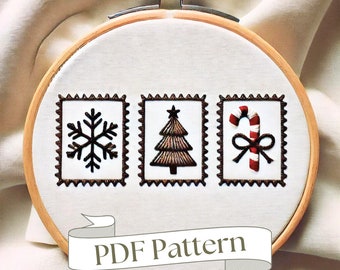 May include: A white embroidery hoop with three brown framed designs. The designs are a snowflake, a Christmas tree, and a candy cane with a bow. The text "PDF Pattern" is written on a brown ribbon banner below the designs.