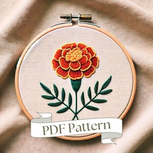 Può includere: Motivo ricamato di margherita in un cerchio. Il fiore è arancione e giallo con foglie verdi e uno stelo. Il cerchio è in legno e ha uno sfondo in tessuto bianco. Il testo "PDF Pattern" è su uno stendardo bianco sotto il cerchio.