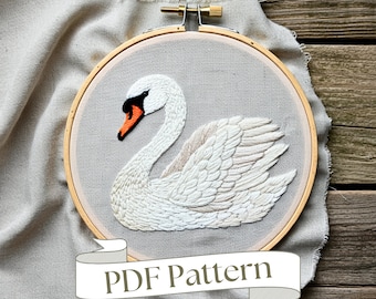 Könnte beinhalten: Gesticktes Schwan-Design in einem Holzreifen. Der Schwan hat weiße und beige Fäden mit einem orangefarbenen Schnabel und schwarzen Akzenten. Der Hintergrund ist ein hellgrauer Stoff. Der Text "PDF Pattern" befindet sich auf einem weißen Banner unten.