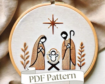 May include: A white embroidery hoop with a brown wooden frame. The hoop features a hand-stitched design of the nativity scene with a star above the manger. The text "PDF Pattern" is displayed on a banner below the design.