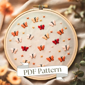 Peut inclure: Gros plan d'un cerceau avec du fil à broder représentant un motif de papillons orange et rose sur un tissu beige. Le cerceau est étiqueté "PDF Pattern".