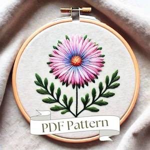 以下が含まれることがあります： 白いリボンに「PDF Pattern」の文字が書かれた、ピンクとブルーの花と緑の葉が描かれた刺繍枠です。