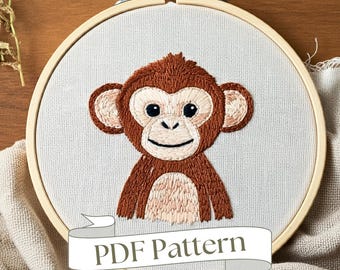 Könnte beinhalten: Stickmuster eines Affen in einem hölzernen Stickrahmen. Der Affe ist braun mit einem hellbraunen Gesicht und einem fröhlichen Ausdruck. Das Muster ist als PDF-Download erhältlich.