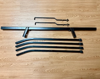 May include: Black metal bed frame components, including a long rectangular headboard support, curved side rails, and two smaller support pieces with hardware. The pieces are arranged on a wood-grain surface.