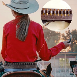 May include: A brown leather belt with 20 ammo loops. The belt is worn by a person wearing a red shirt and a light gray cowboy hat. The person is riding a brown horse. The belt has a decorative floral pattern.