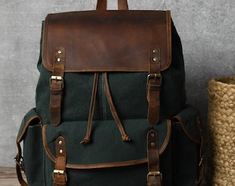 May include: A dark green canvas backpack with brown leather accents and buckles. The backpack has a drawstring closure and two side pockets.