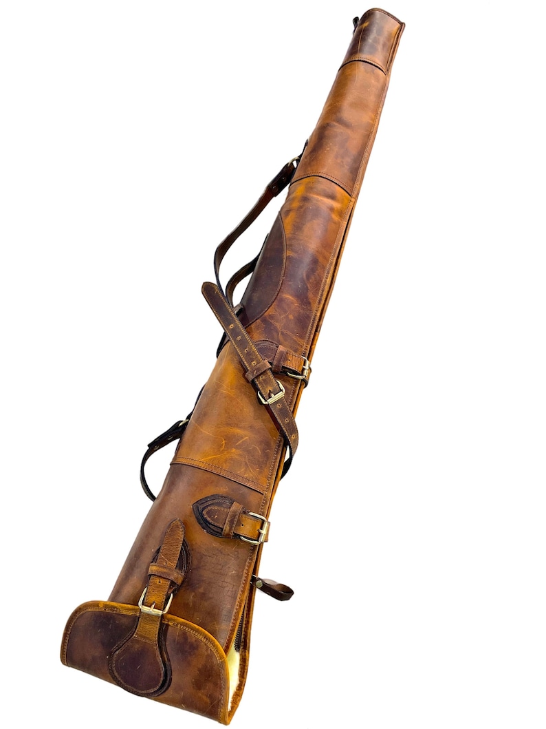 May include: A brown leather gun case with multiple straps and buckles. The case has a soft, fuzzy lining.