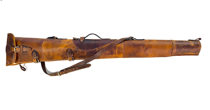 May include: A brown leather gun case with a shoulder strap and buckles. The case is made of distressed leather and has a rustic look.