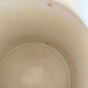 May include: White enamelware pot with a slight chip on the rim. The interior of the pot is white and shows signs of use.