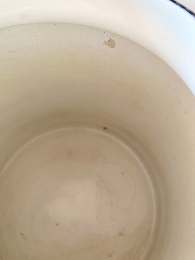 May include: White enamelware pot with a slight chip on the rim. The interior of the pot is white and shows signs of use.