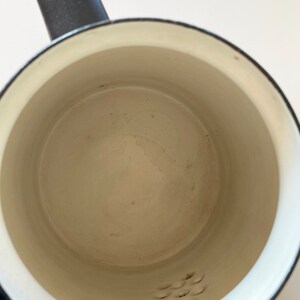 May include: A white enamel saucepan with a black handle and a small strainer on the bottom.