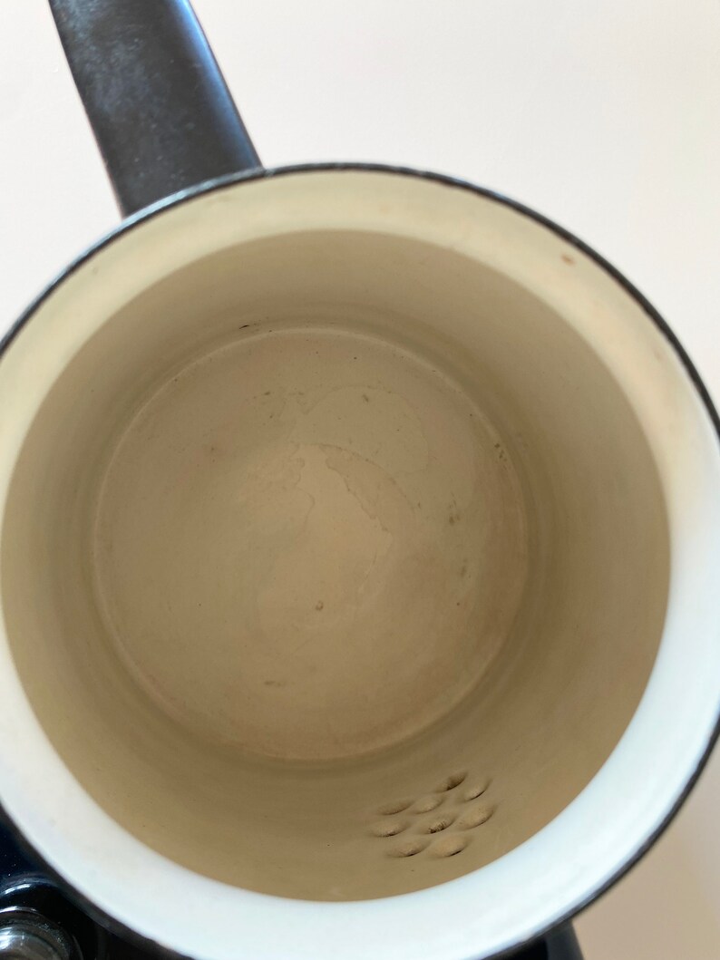 May include: A white enamel saucepan with a black handle and a small strainer on the bottom.