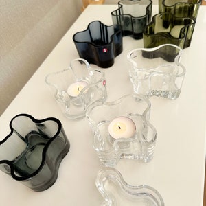 May include: A set of eight glass candle holders in various colors, including clear, gray, and green. The holders are shaped like a stylized flower with multiple rounded petals. Some of the holders have a tealight candle inside.