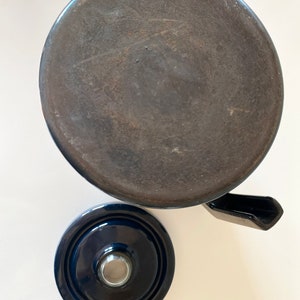 May include: A dark blue ceramic teapot with a lid and a spout. The teapot is sitting on a white surface.