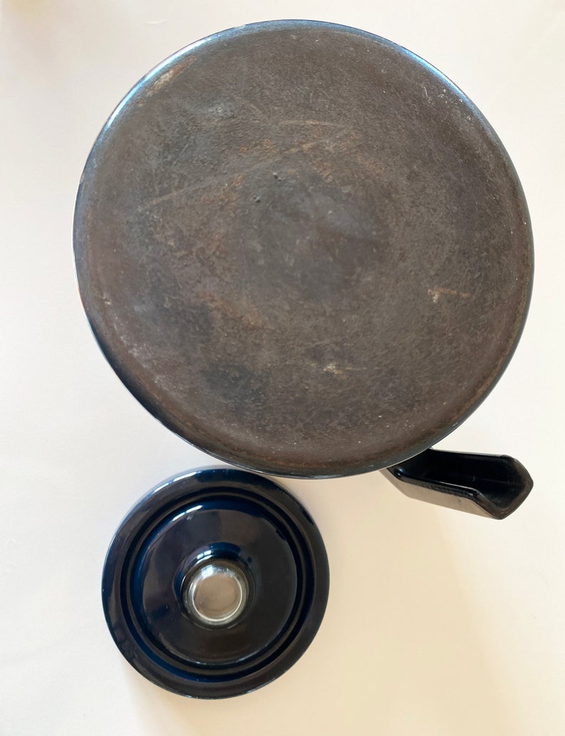 May include: A dark blue ceramic teapot with a lid and a spout. The teapot is sitting on a white surface.