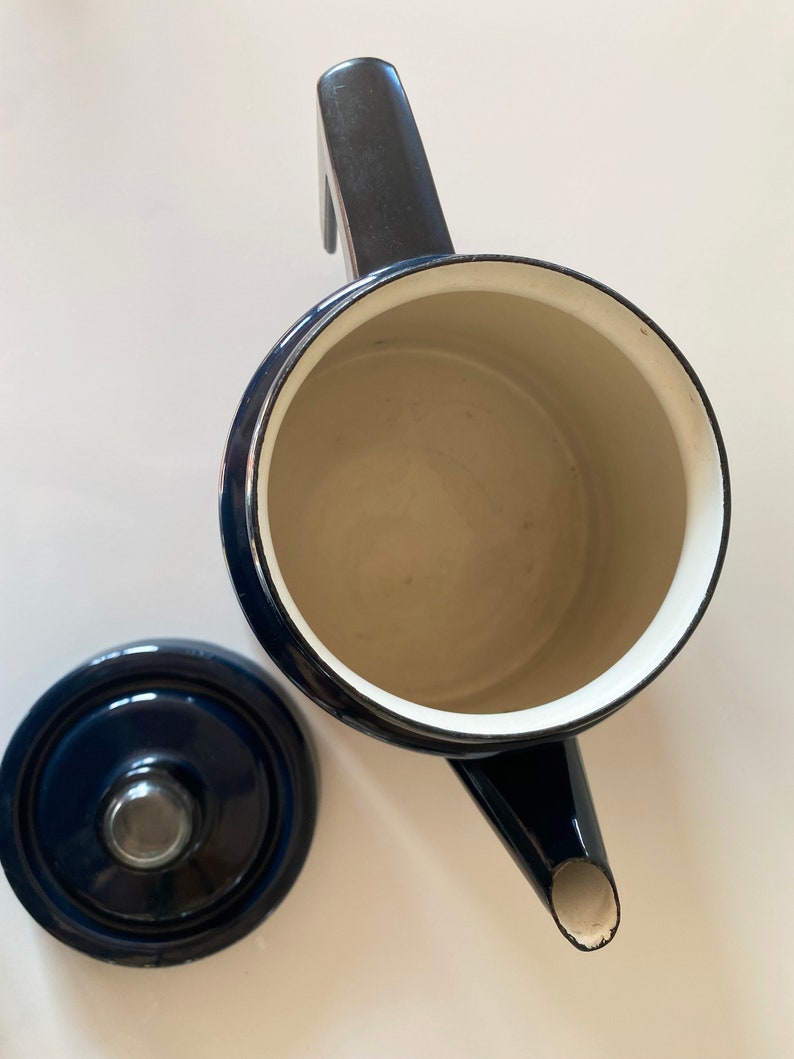 May include: A blue enamel teapot with a black handle and a white interior. The teapot has a spout and a lid. The lid is also blue enamel with a black knob.