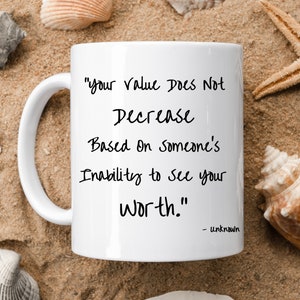 Puede incluir: Taza de café de cerámica blanca con una cita inspiradora en negro que dice "tu valor no disminuye en función de la incapacidad de alguien para ver tu valor." La cita se atribuye a "desconocido".