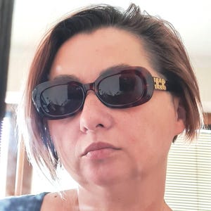 May include: Oval tortoiseshell sunglasses with dark lenses. The temples have gold-coloured decorative accents. A classic accessory, suitable for various styles and occasions.
