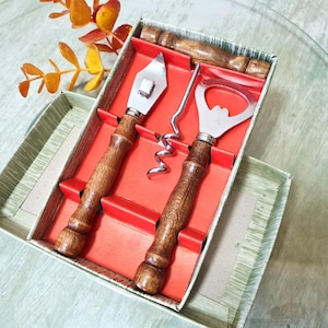 Puede incluir: Un juego de herramientas de bar vintage con mangos de madera y cabezales de acero inoxidable. El juego incluye un abridor de botellas, un sacacorchos y un abrelatas, presentado en una caja forrada en rojo. Los mangos tienen un acabado de vetas de madera rico.