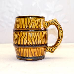 Peut inclure: Une chope en céramique marron avec un motif de tonneau. La chope a une anse et est décorée de bandes marron foncé et de lignes verticales pour imiter le grain du bois. La chope mesure environ 10 cm de haut.