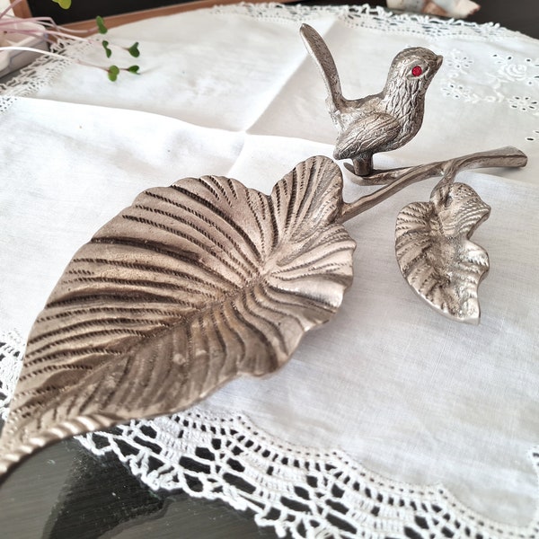 L'un des 2 plateaux en métal argenté représentant un oiseau sur une branche avec une feuille, un porte-gobelet ou un porte-bougie, cendrier décoratif en laiton