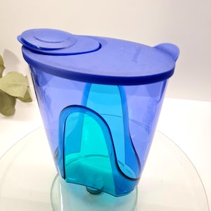 Può includere: Una brocca d'acqua in plastica blu con coperchio abbinato. La brocca ha un interno trasparente color turchese e un manico laterale. Il coperchio ha una piccola apertura circolare per versare.