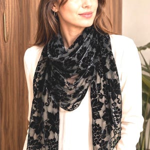 May include: A black velvet scarf featuring a semi-sheer base with a raised, textured floral and grape cluster pattern. The fabric has a soft, plush finish on the velvet elements, creating a distinct contrast against the translucent background material.